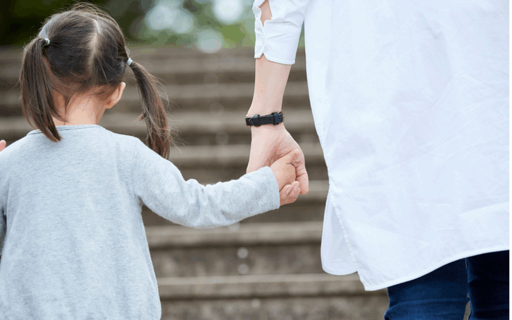 Das Bild zeigt eine Frau, die die Hand eines Mädchens festhält, während die beiden spazieren gehen.